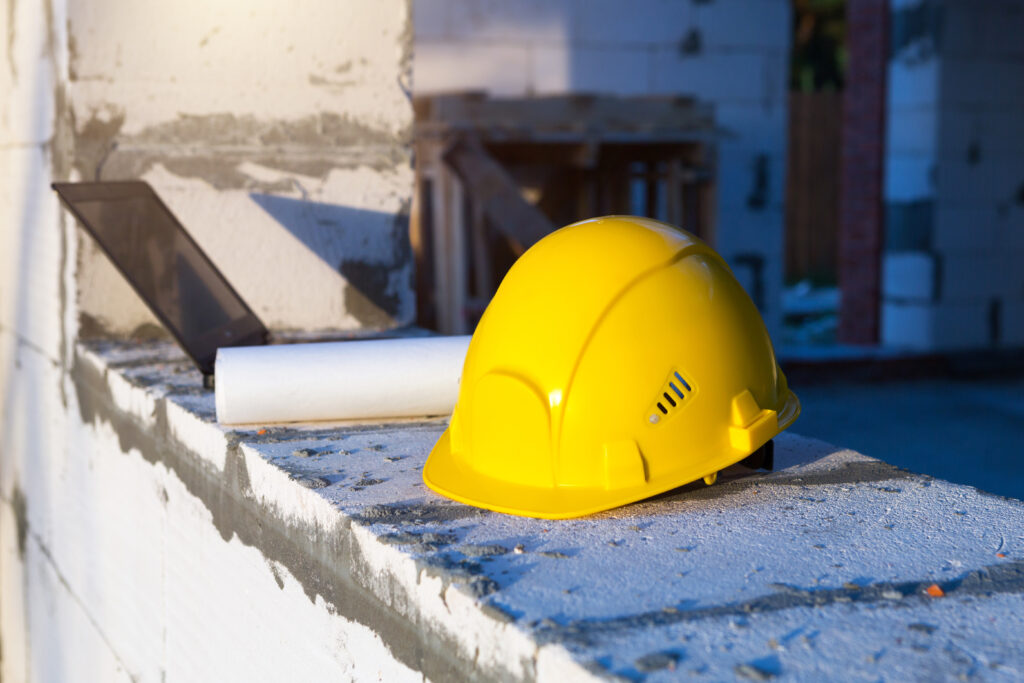 Construction hardhat, drawing and laptop on the window of a house under construction